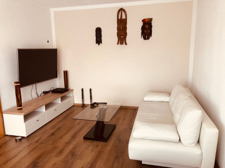 Wohnbereich mit weißem Ledersofa, Glascouchtisch und Holzmasken an der Wand