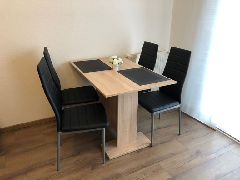 Zona pranzo con tavolo in legno chiaro e quattro sedie nere vicino alla finestra